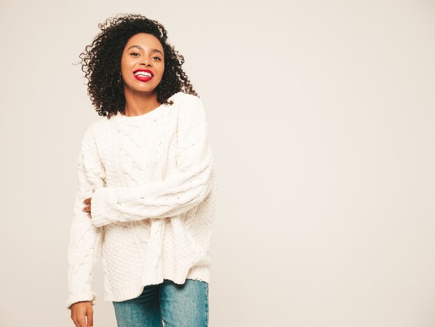 Linda mulher negra com penteado afro cachos e lábios vermelhos. Modelo sorridente em roupas da moda jeans e suéter de inverno.