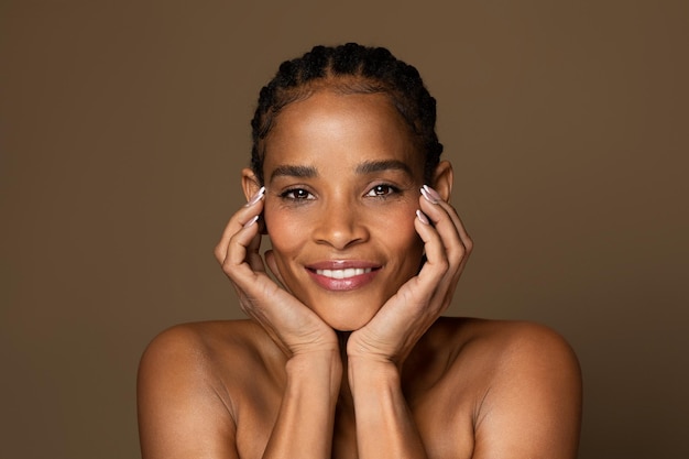 Foto linda mulher negra de meia-idade tocando seu rosto e sorrindo para a câmera desfrutando de tratamentos de beleza