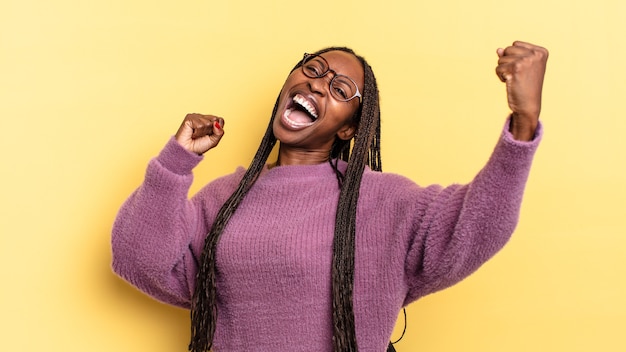 Linda mulher negra e negra gritando triunfantemente, parecendo vencedora animada, feliz e surpresa, comemorando