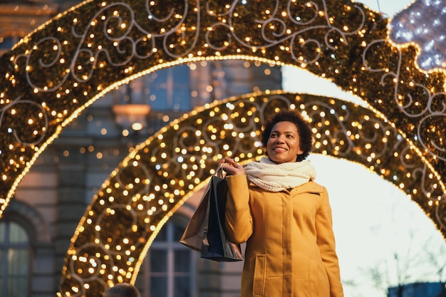 Linda mulher negra sorridente andando e fazendo compras durante as férias de Natal na cidade.