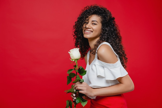 Linda mulher negra sorrindo com rosa branca isolada sobre vermelho