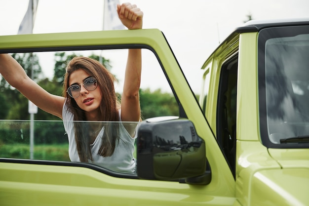 Linda mulher no carro verde moderno, posando para a câmera.