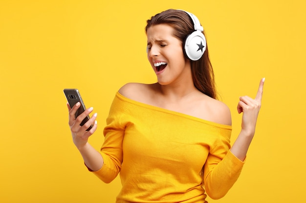 linda mulher ouvindo música no celular sobre amarelo