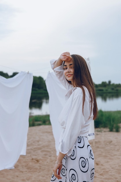 Foto linda mulher parada perto de roupa branca secando na natureza no verão