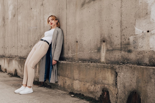 Linda mulher posando perto da parede cinza. Garota vestida com roupas casuais com lábios vermelhos. moda, maquiagem