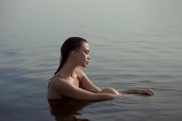 Linda mulher romântica sentada perto de um lago lagoa Mulher molhada em sua cueca sob os raios do sol ao pôr do sol Beleza natural cabelos longos