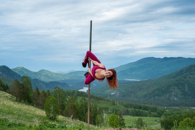 Linda mulher ruiva dançando em uma plataforma portátil em um fundo de montanhas A garota se move sexualmente ao lado do mastro Macacão para aulas de salto alto Altai Flexibilidade impressionante