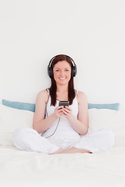 Linda mulher ruiva ouvindo música com seus fones de ouvido enquanto estava sentada na cama