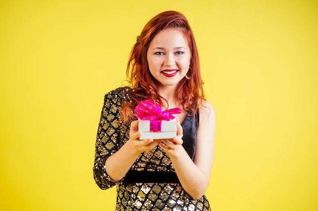Linda mulher ruiva segurando uma caixa de presente em um fundo amarelo em estúdio