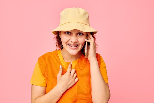 Linda mulher se comunica ao telefone em chapéu amarelo moda fundo rosa inalterado