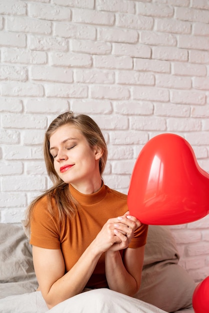 Linda mulher segurando o balão vermelho em forma de coração sentado na cama