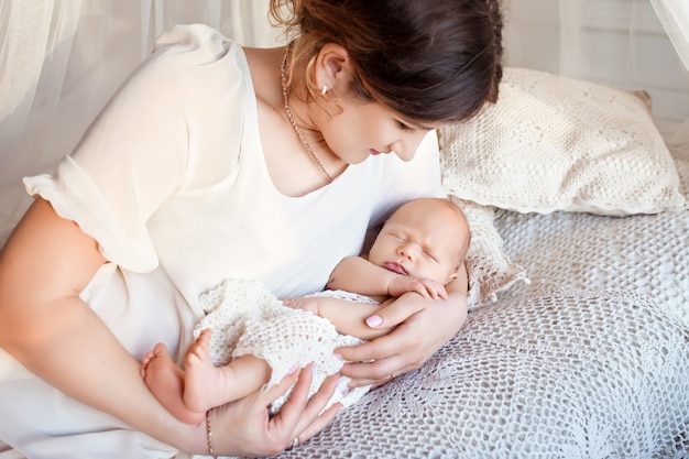 Linda mulher segurando um bebê recém-nascido nos braços. mãe feliz e seu bebê recém-nascido escorregando na cama