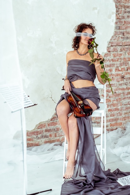 Foto linda mulher segurando um violino e cheirando a rosa vermelha