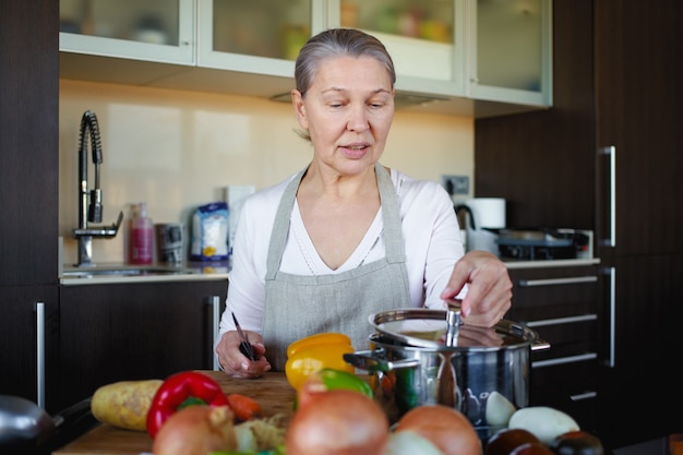 Foto linda mulher sênior com avental na cozinha preparando comida