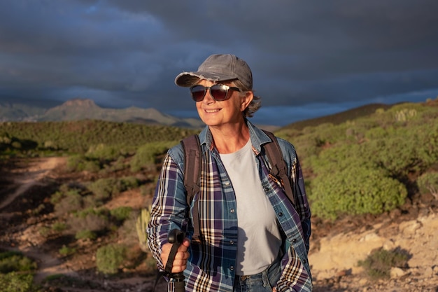 Linda mulher sênior de chapéu e roupas esportivas em dia de caminhada caminhando ao pôr do sol desfrutando de liberdade