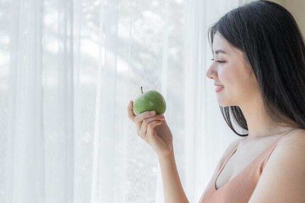 Linda mulher sexy de beleza magra segurando maçã verde no fundo do quarto branco