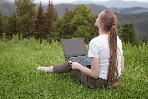 Linda mulher sonhadora com um laptop sentado em gras verdes