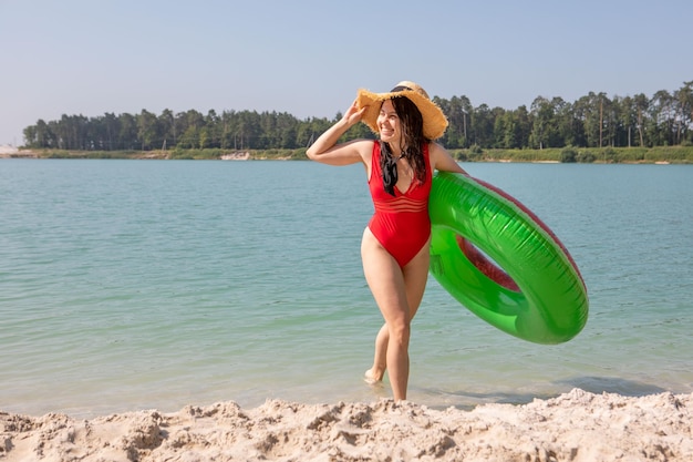 Linda mulher sorridente com anel inflável saindo do lago com água azul