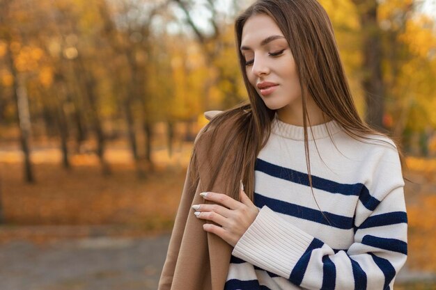 Linda mulher sorridente com roupa elegante, sentada à mesa com um chapéu e um suéter, humor romântico feliz, esperando um namorado para um encontro em um café, tendência da moda primavera-verão, bebendo café