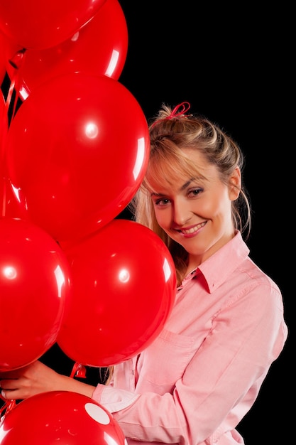 Linda mulher sorridente na blusa rosa segurando balões vermelhos em fundo preto