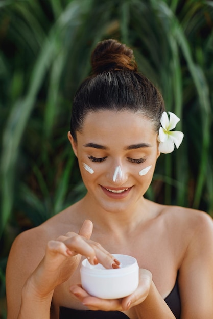 Linda mulher sorrindo retrato de beleza do rosto feminino segurando e aplicando creme cosmético cuidados com a pele