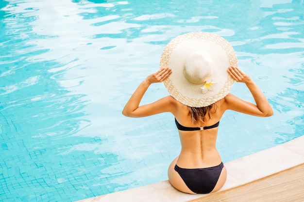 Linda mulher tocando o chapéu e curtindo uma piscina no resort