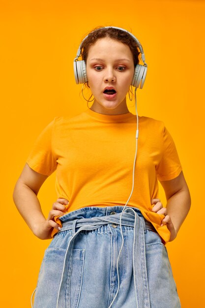 Linda mulher usando fones de ouvido shorts jeans closeup emoções fundo amarelo inalterado