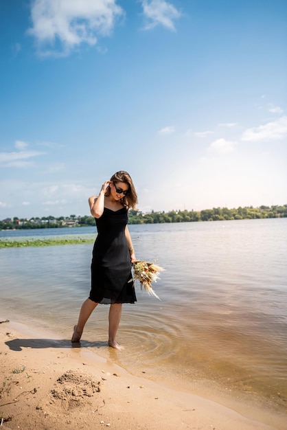 Linda mulher usando vestido preto coquetel em pé no lago de água