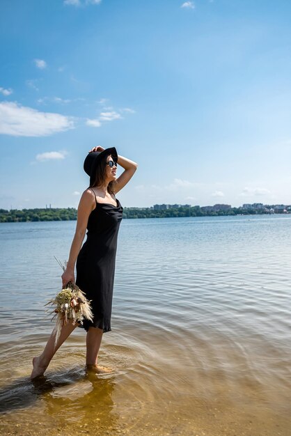 Linda mulher usando vestido preto coquetel em pé no lago de água
