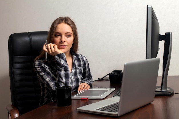 Linda mulher vai fazer seu trabalho de retoque sentada na cadeira usando laptop no escritório