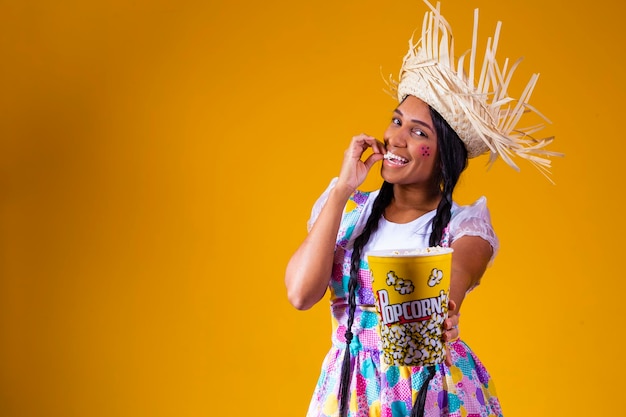 Foto linda mulher vestida com roupa de festa junina comendo pipoca