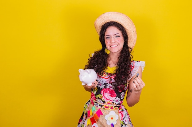 Linda mulher vestida com roupas típicas para uma Festa Junina Segurando cofrinho e moeda