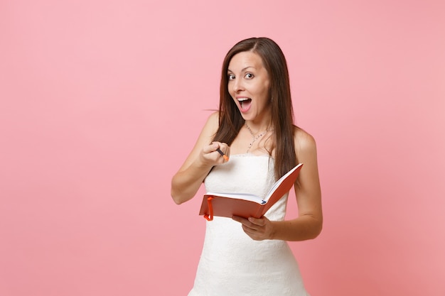 Linda mulher vestida de branco segurando o diário, o caderno e apontando o lápis para a frente