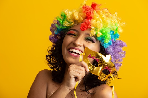 Linda mulher vestida para a noite de carnaval. Mulher sorridente pronta para curtir o carnaval com uma peruca e máscara coloridas