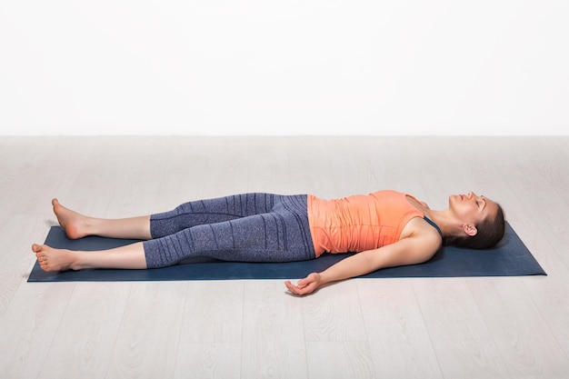 Linda mulher yogini de ajuste esportivo relaxa na pose de cadáver de yoga asana Savasana no estúdio