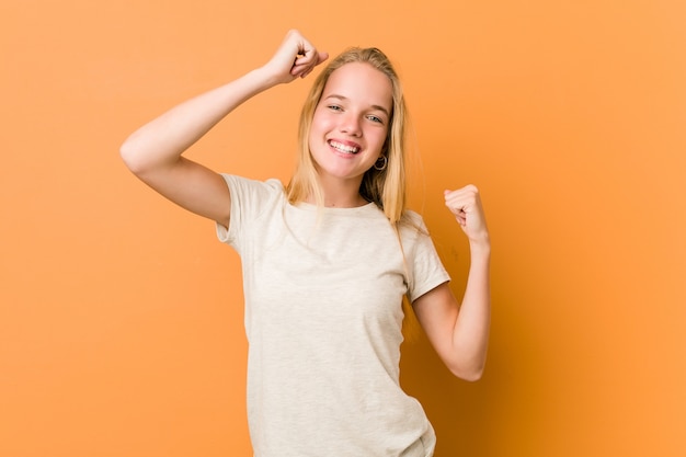 Linda y natural mujer adolescente celebrando un día especial, salta y levanta los brazos con energía.