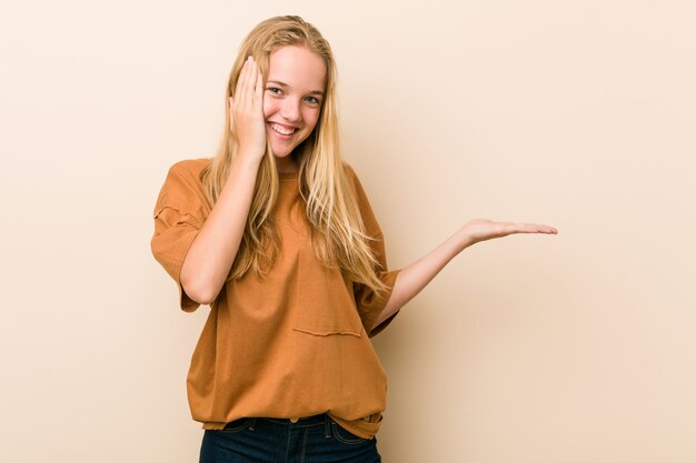 Linda y natural mujer adolescente tiene espacio de copia en una palma, mantenga la mano sobre la mejilla. Sorprendido y encantado.