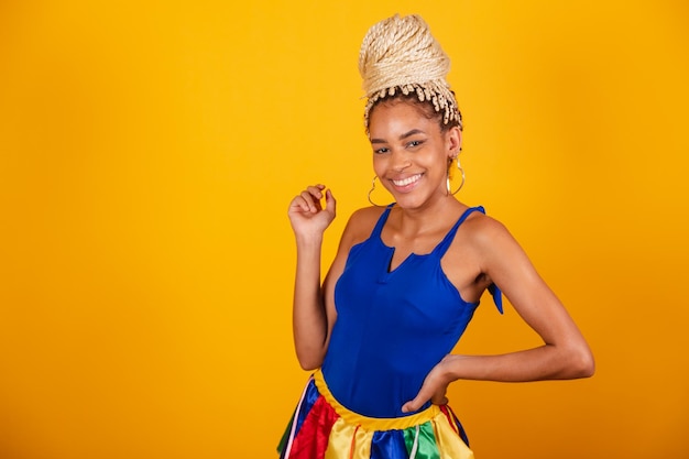 Linda negra brasileira vestida com roupas de carnaval coque de fundo azul e amarelo e tranças com as mãos na cintura