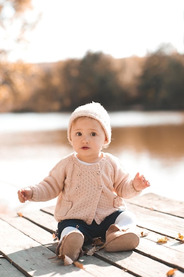 Linda niña de 1 año con ropa de punto elegante posando en el parque de  otoño al aire libre mirando a la cámara