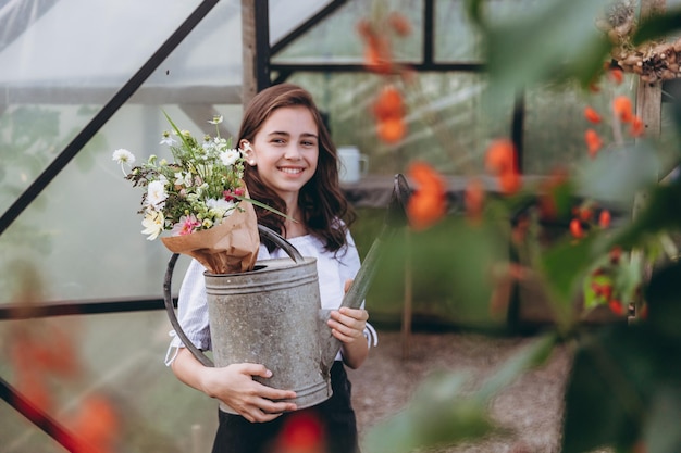 Linda niña de 13 años que lleva una cesta de flores hermosas en el campo de flores con felicidad