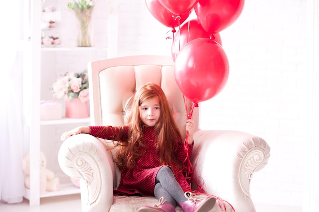 Linda niña de 3 a 4 años sosteniendo globos rojos en la habitación Celebración del feliz cumpleaños