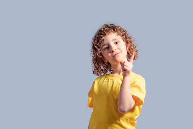 Linda niña de 5 años con camiseta amarilla girando la cabeza en gris