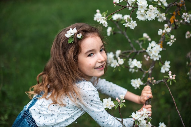 Una linda niña de 5 años en un floreciente huerto de manzanas blancas en primavera. Primavera, huerta, floración, alergia, fragancia primaveral, ternura, cuidado de la naturaleza. Retrato