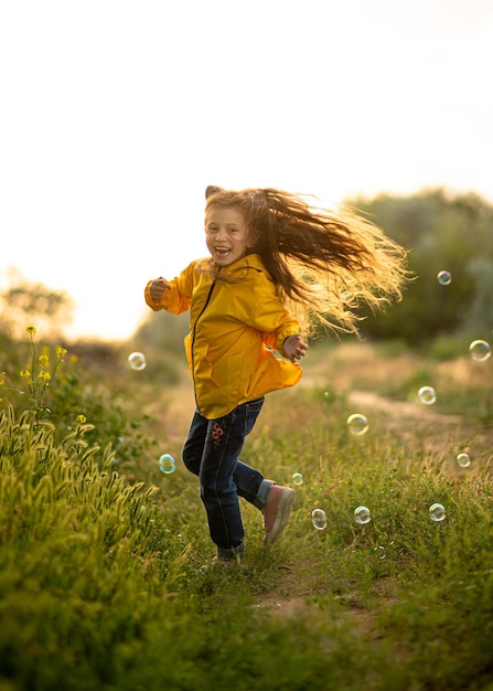 Una linda niña de 5 años en un parque amarillo juega y se divierte con pompas de jabón al atardecer. Infancia. Luz de sol. Descanso en familia en la naturaleza.