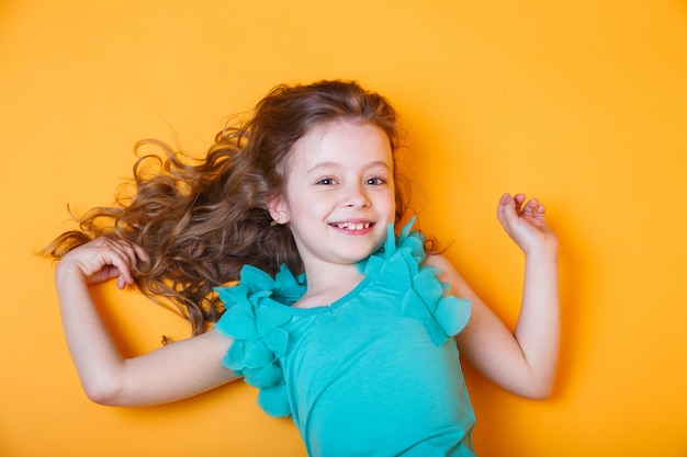 Linda niña de 7 años en blusa azul sobre fondo naranja