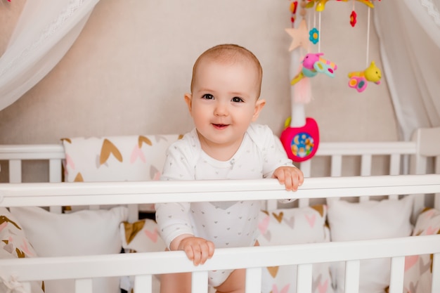 Linda niña de 8 meses se sienta en la cama de bebé en casa