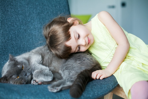 Linda niña abrazando a su gato británico gris