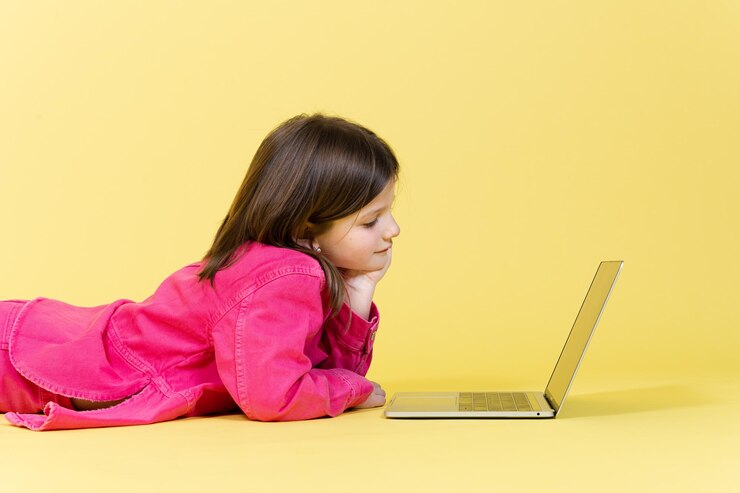 Foto linda niña acostada en el piso y concentrada en la computadora portátil