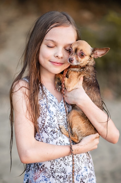 Linda niña adolescente abraza a su perro. Retrato de un niño con un chihuahua. Una niña de pelo largo muestra amor y tiernos sentimientos por una mascota. Un perro de pura sangre en manos de su dueño.