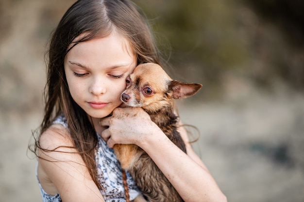 Linda niña adolescente abraza a su perro. Retrato de un niño con un chihuahua. Una niña de pelo largo muestra amor y tiernos sentimientos por una mascota. Un perro de pura sangre en manos de su dueño.